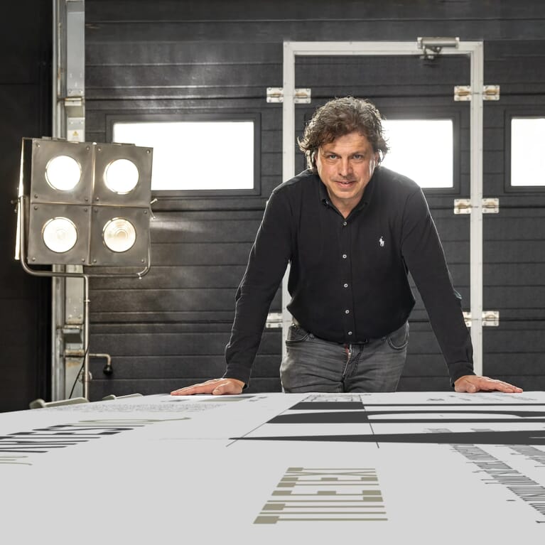 Man leunt op een tafel en kijkt naar de camera