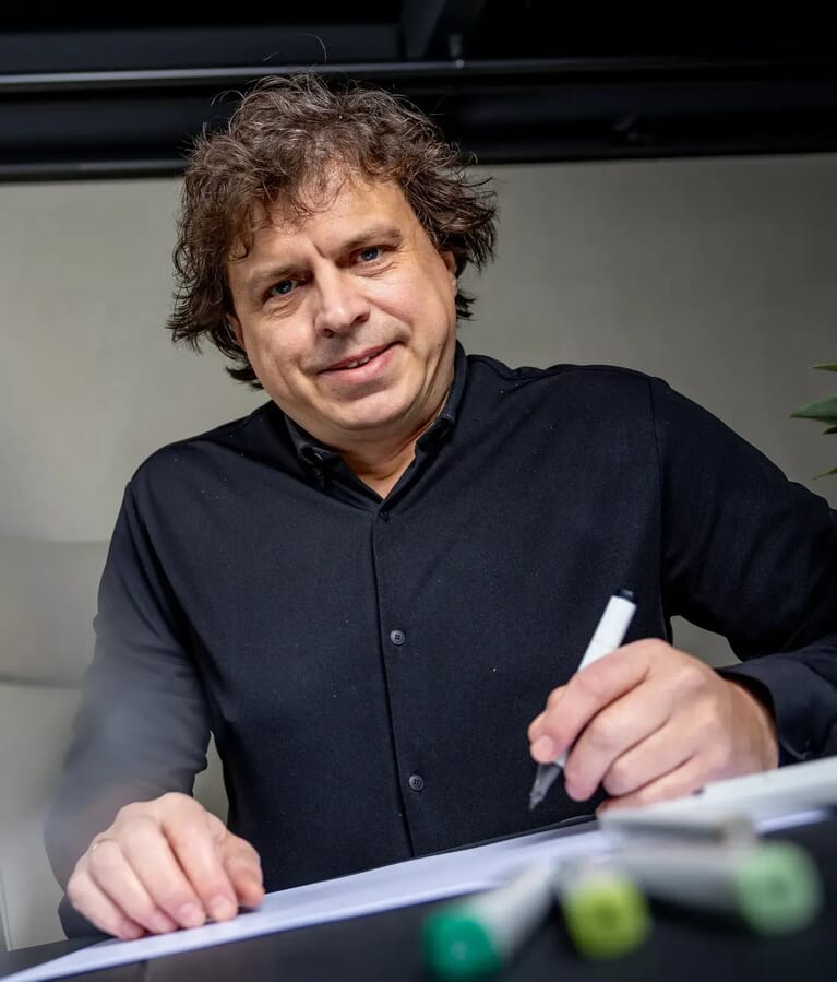 Man tekent iets op papier en lacht naar de camera