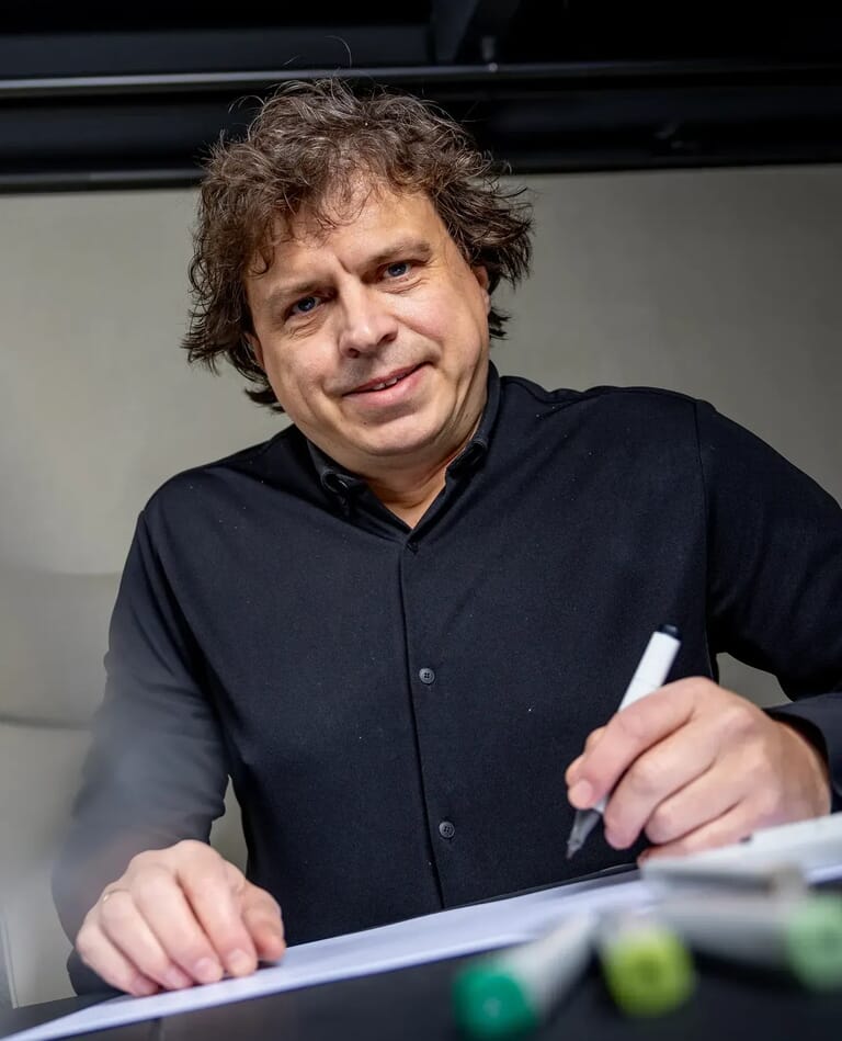 Een man tekent op een papier en kijkt de camera in