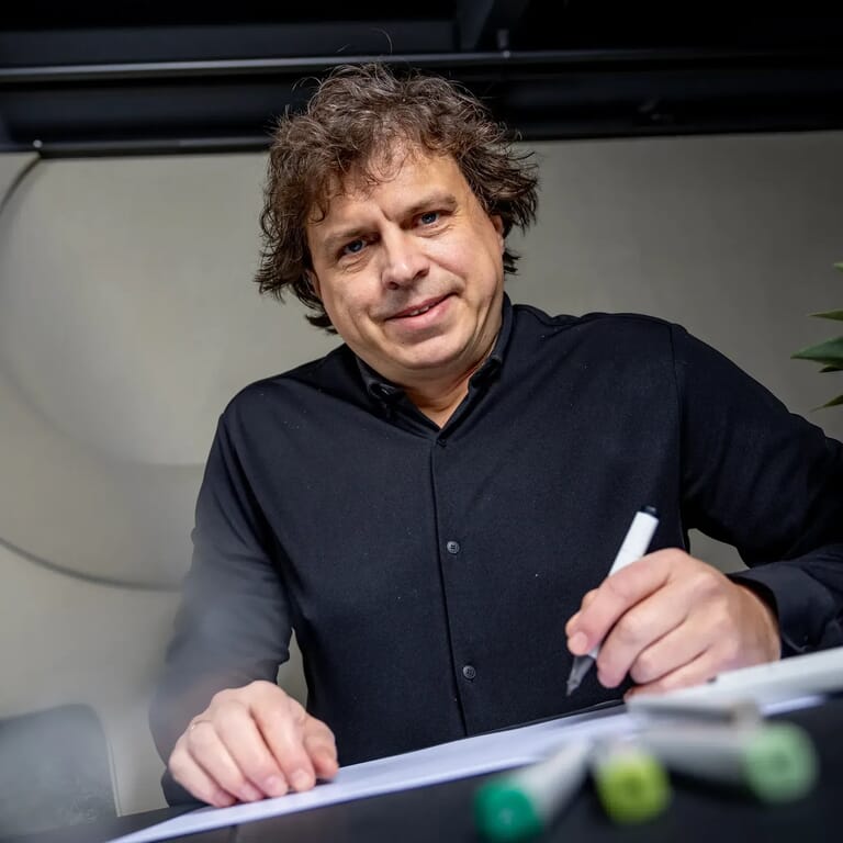 Man tekent op een papier en kijkt de camera in