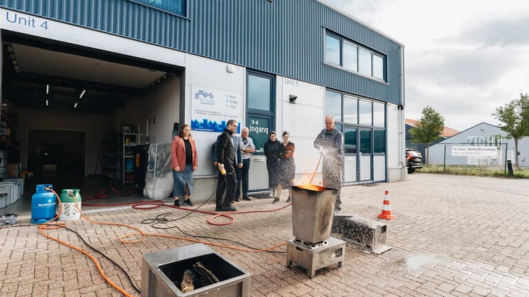 Groep mensen op een terrein met een brandende bak en iemand die het blust