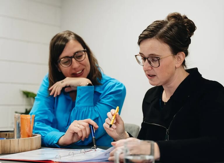 Twee vrouwen aan tafel kijken naar papieren op tafel