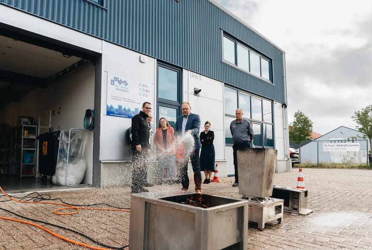 Een groep mensen kijken naar hoe een man een brand in een stalen doos blust