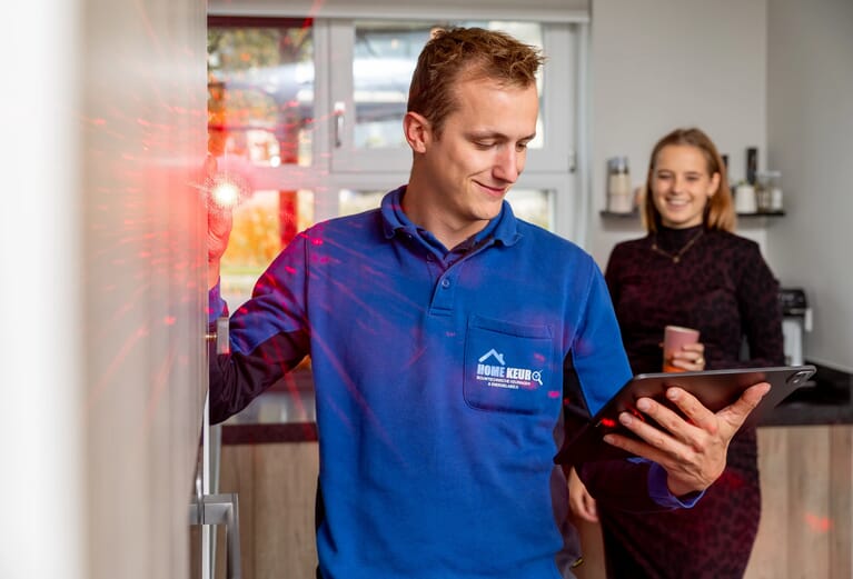 Man schijnt met een laser in de camera en kijkt op tablet, op de achtergrond is een vrouw te zien