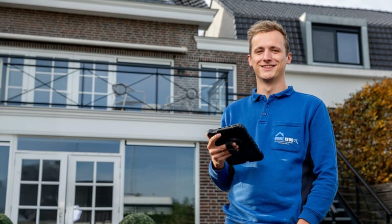Een man voor een huis met een tablet in zijn hand