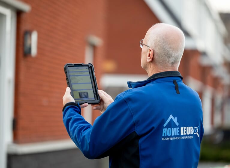 Een man heeft een tablet in de hand en kijk naar een huis