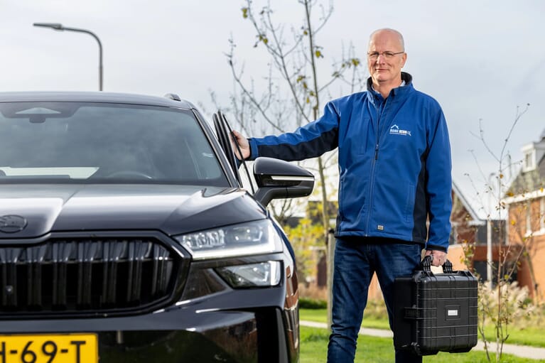 Man die een autodeur sluit en een zwarte koffer in zijn hand