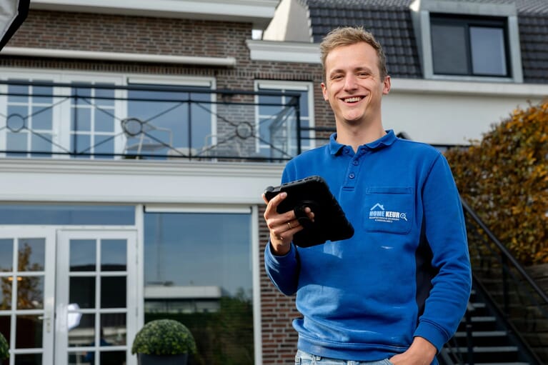 Een man staat voor een huis met een tablet en lacht