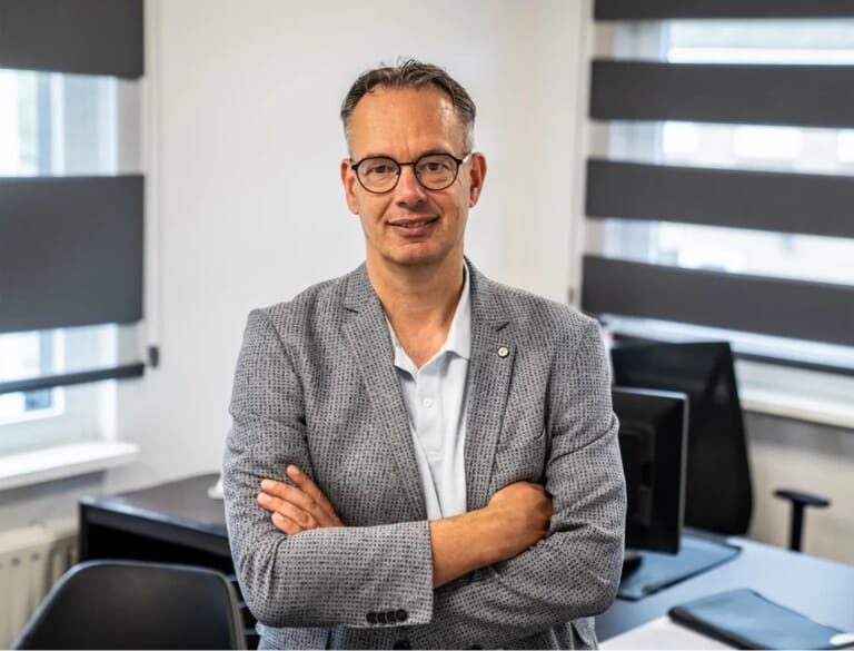 Een man met zijn armen over elkaar voor een bureau