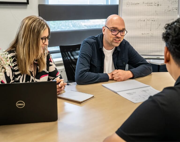 Drie mensen aan een tafel met een laptop en een document