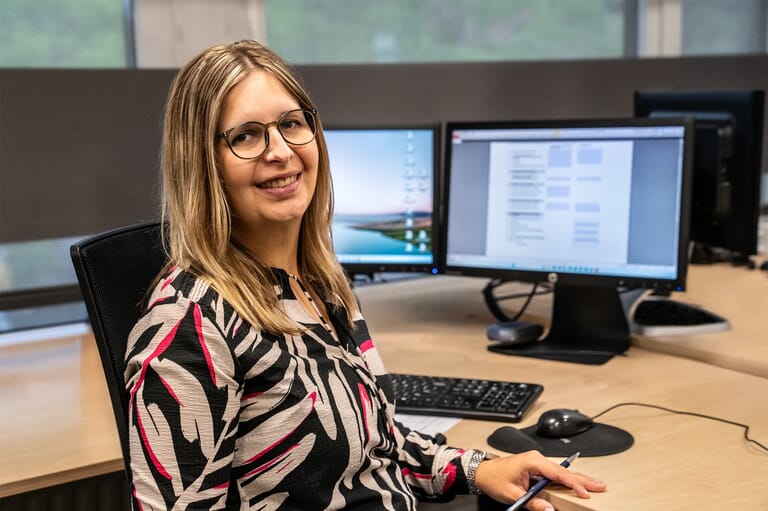 Een vrouw die voor een bureau zit met een open beeldscherm