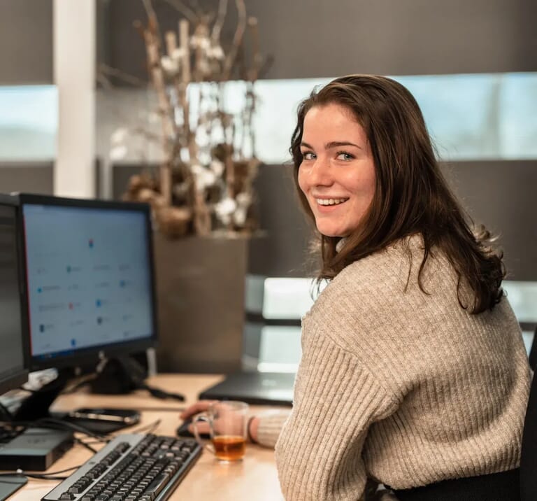 Vrouw achter een laptop en kijkt in de camera