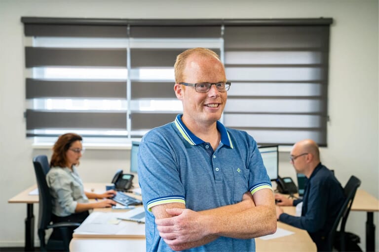 Een man met zijn armen over elkaar voor een werkruimte