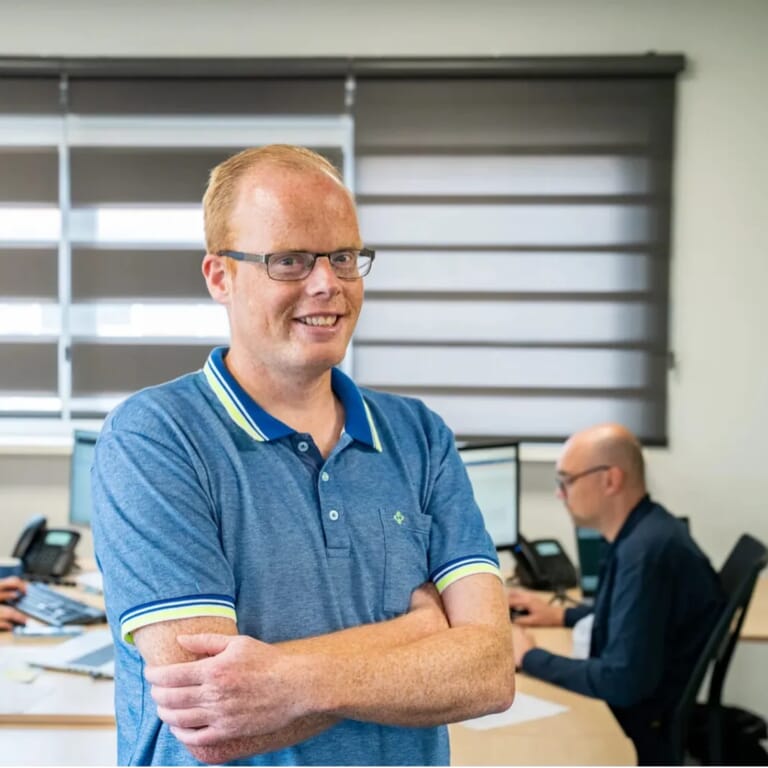 Een man met zijn armen over elkaar voor een werkruimte