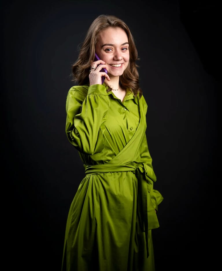 Een vrouw met bruin haar in een groene jurk met een telefoon aan haar oor
