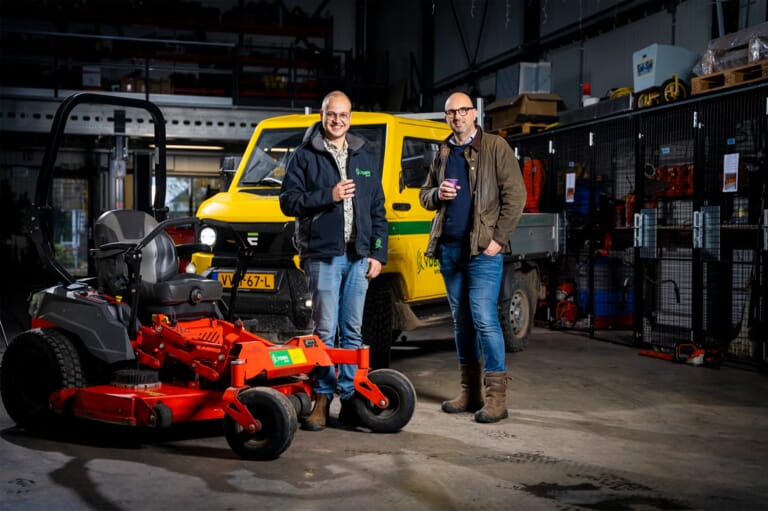 Twee mannen in een werkplaats met voertuigen en gereedschap