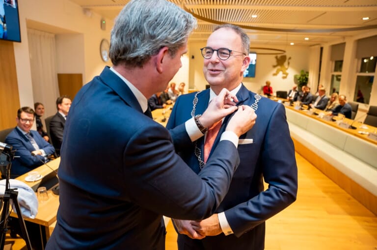 Twee mannen in een vergaderzaal waar de ene man iets opspeld bij de ander