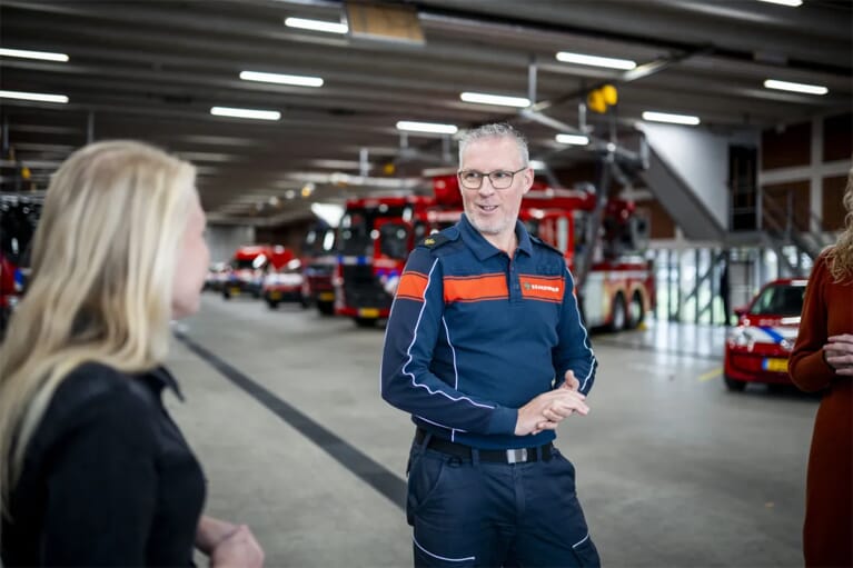 Een brandweerman in een hal met bluswagens