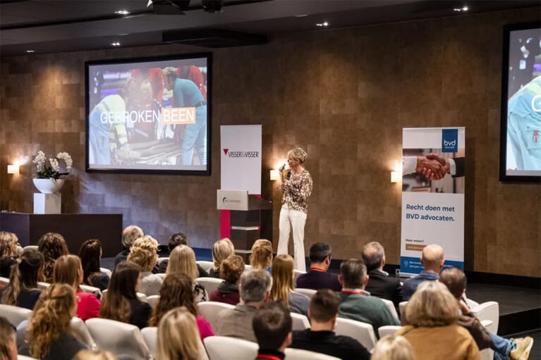 Een bijeenkomst met op het podium een vrouw