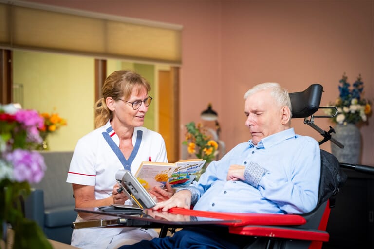 Een vrouw leest een boek voor aan een man in een rolstoel