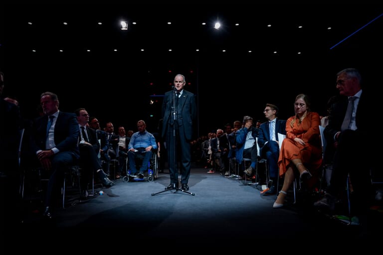 Een man in pak in een zaal met zittende mensen