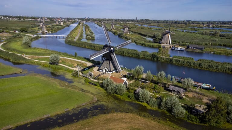 Een molen met een huis en tuin in de polder in een landschap met dijken en water
