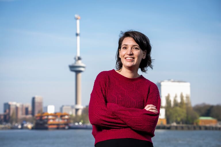 Een vrouw met de handen over elkaar voor de skyline van Rotterdam