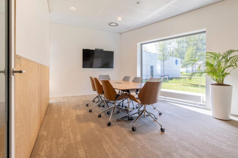 Moderne vergaderruimte met tafel, stoelen, scherm en raam.