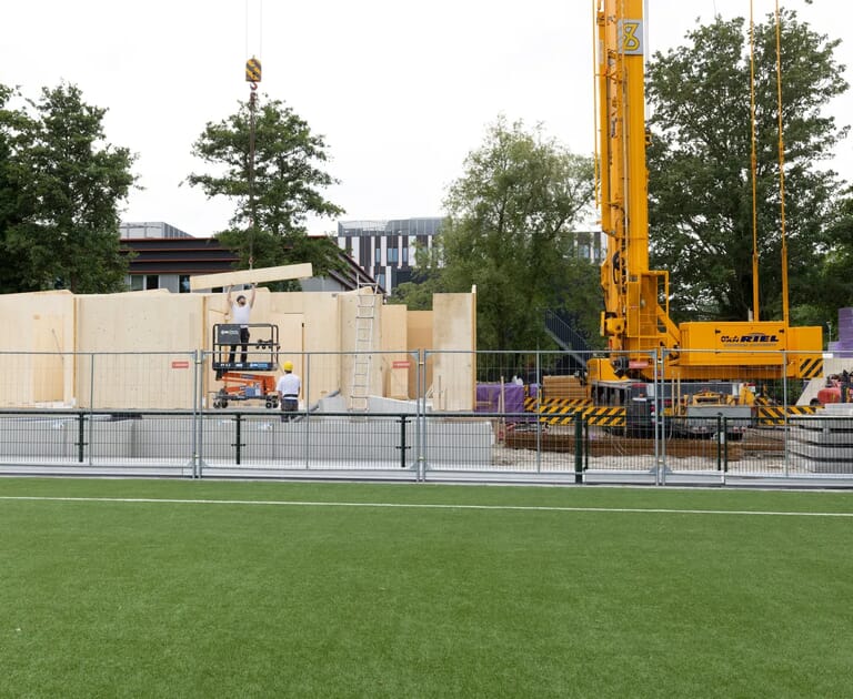 Bouwplaats met gele kraan en houten muren in opbouw.