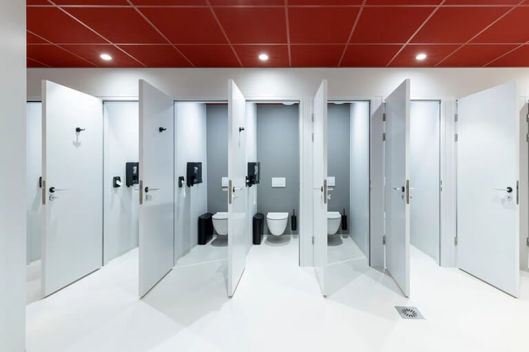 Open toilethokjes in een moderne badkamer met rode plafondtegels.