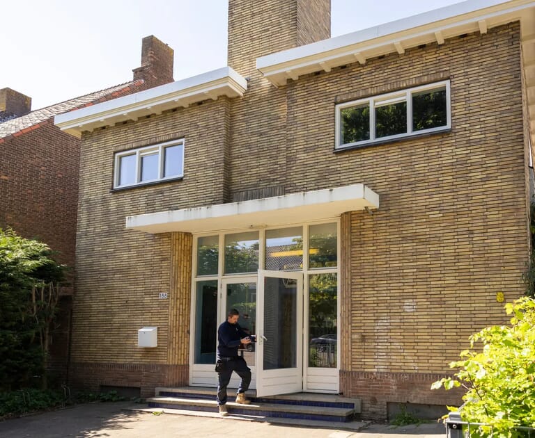 Man bij voordeur van een bakstenen huis met grote ramen