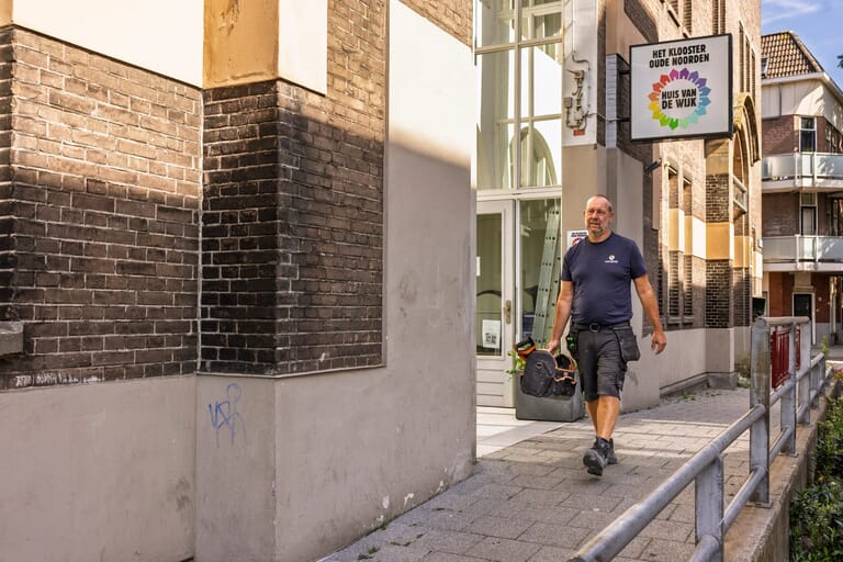 Man loopt met gereedschap voor gebouw 'Huis van de Wijk'.