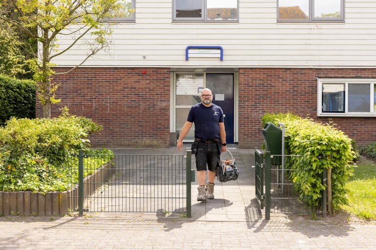 Man met gereedschap voor een huis met rode bakstenen en witte gevel.