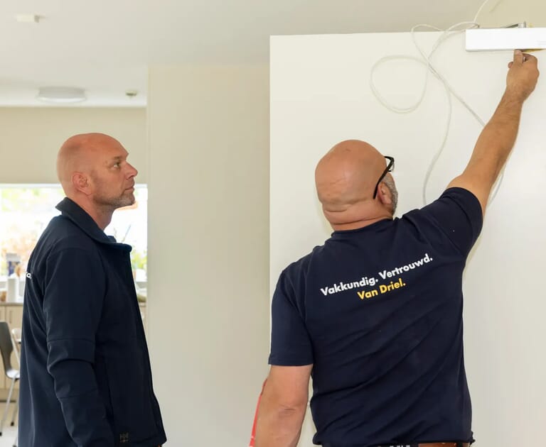 Twee mannen werken samen aan een wit paneel binnen in huis