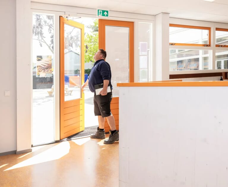 Man inspecteert een nooddeur in een licht kantoor.