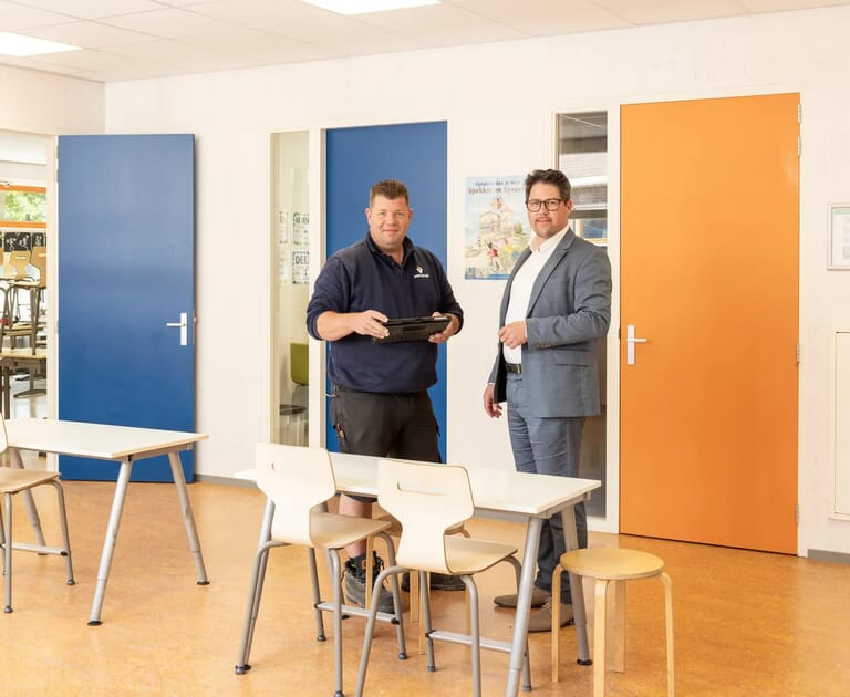 Twee mannen staan in een klaslokaal met kleurrijke deuren.