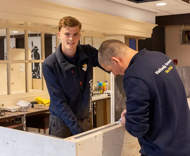 Twee mannen werken samen aan een bouwproject binnen.