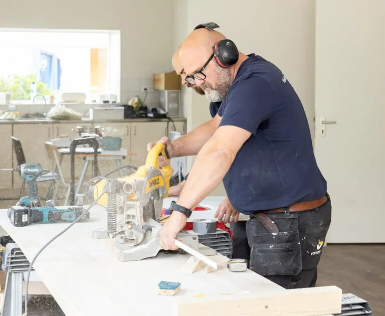 Man bedient zaagmachine in werkplaats.