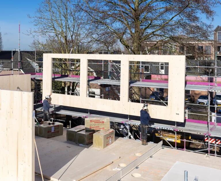 Twee arbeiders installeren een houten muur op een bouwplaats.