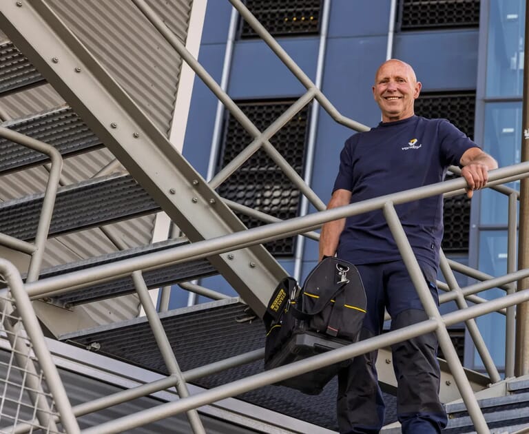 Man met gereedschapstas op een buitentrap bij een gebouw