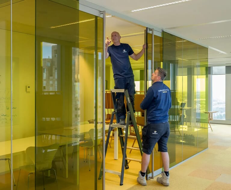 Twee mannen installeren glazen wanden in een kantoorruimte.