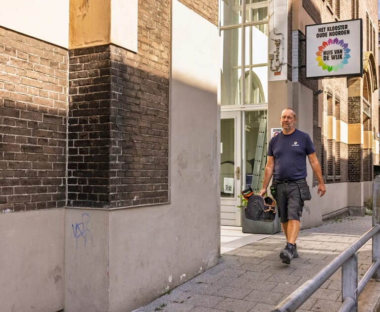 Man met gereedschapstas loopt langs een gebouw met 'Huis van de Wijk' bord.