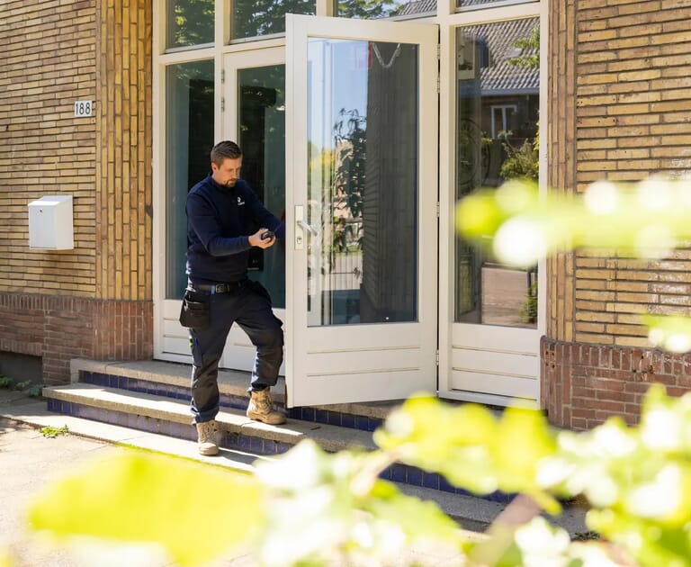 Persoon in werkkleding sluit een deur van een gebouw.