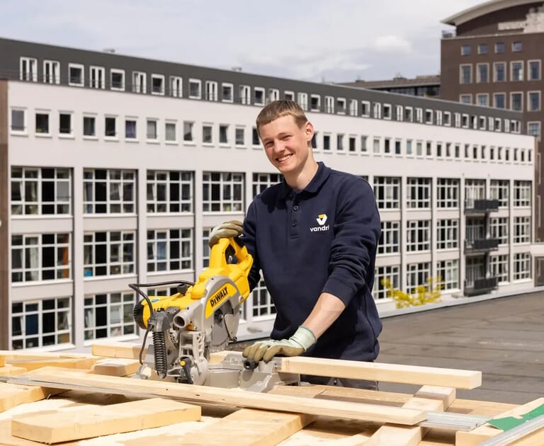Jonge man zaagt hout op een dak