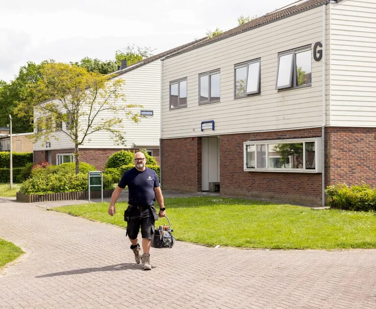 Man met gereedschapstas loopt voor een woonblok