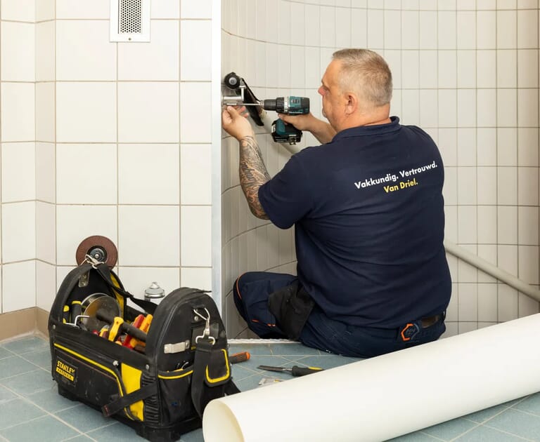 Monteur met gereedschapstas installeert douche in betegelde badkamer.