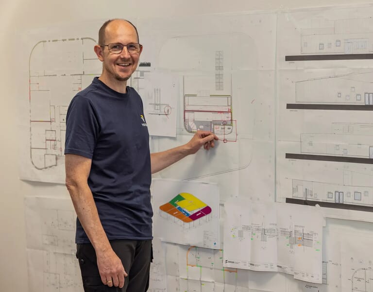 Man wijst naar bouwtekening aan muur.