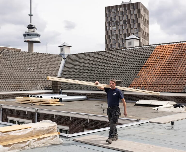 Man draagt platen hout op een dak met stadsachtergrond
