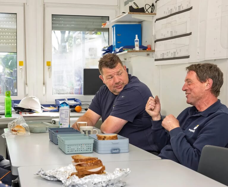 Twee mannen in pauzeruimte praten tijdens lunch met sandwiches.