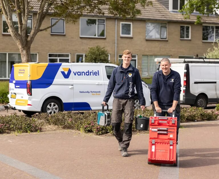 Twee mannen met gereedschap en busje van Van Driel op de achtergrond.